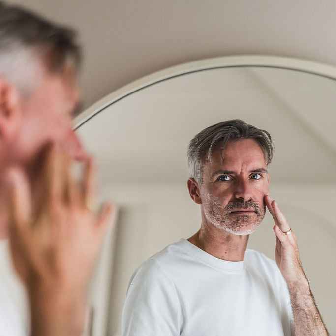 Man bij de spiegel brengt oogcrème aan