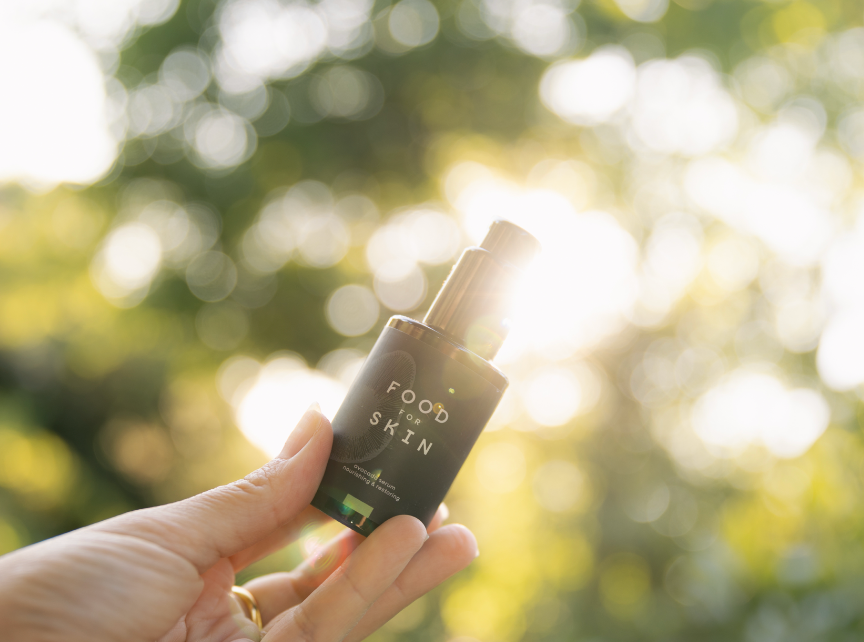Hand met Avocado Serum voor boom waar zonlicht doorheen valt