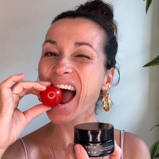 Vrouw bijt in een tomaat en houdt een pot crème vast