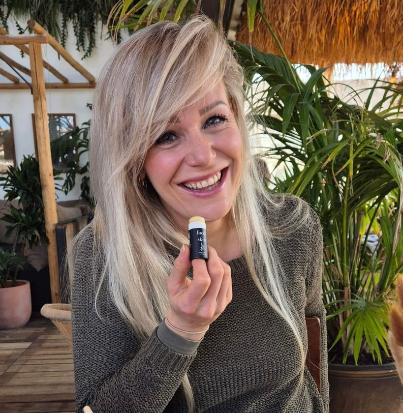 Vrouw houdt een Food for Skin lipbalm vast tussen planten