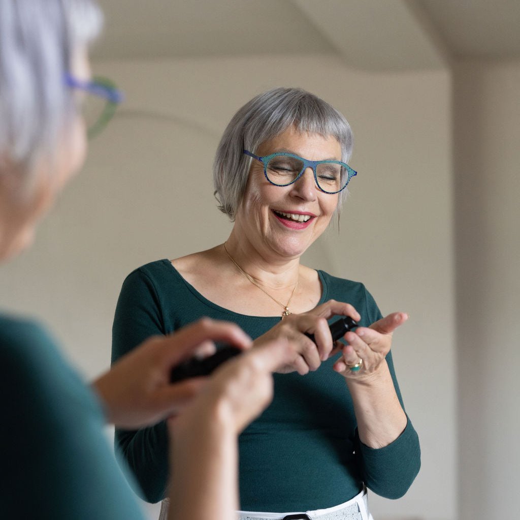 Vrouw met kort grijs haar bij de spiegel, met een flesje serum