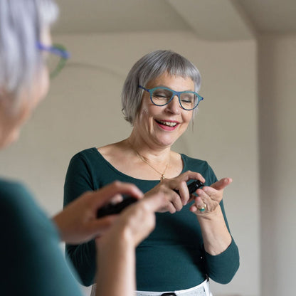 Vrouw met kort grijs haar bij de spiegel, met een flesje serum